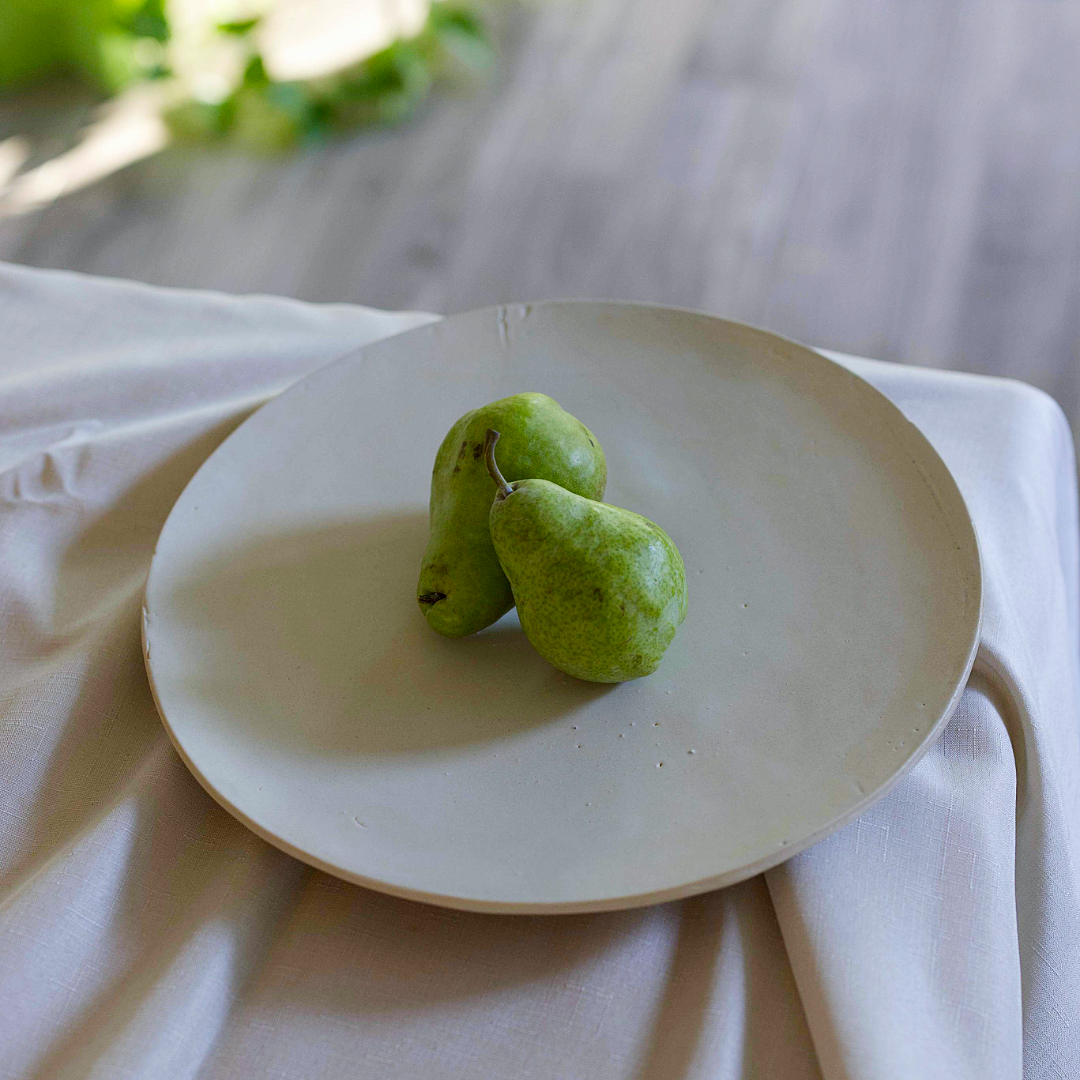 Two green fruits on a white plate with a blurred background
